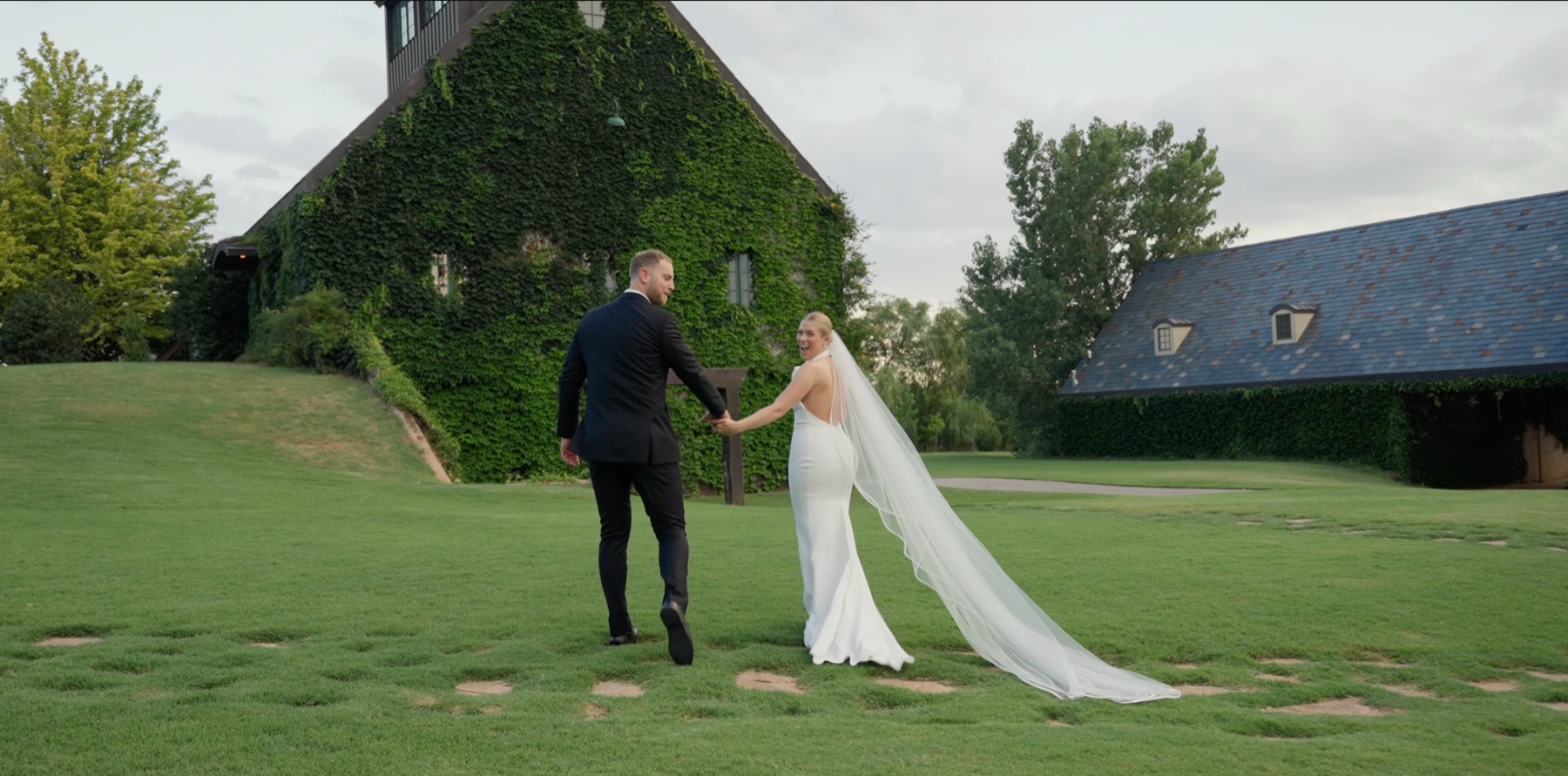 Bride looking back over her shoulder as she and the groom walk hand in hand across a lawn