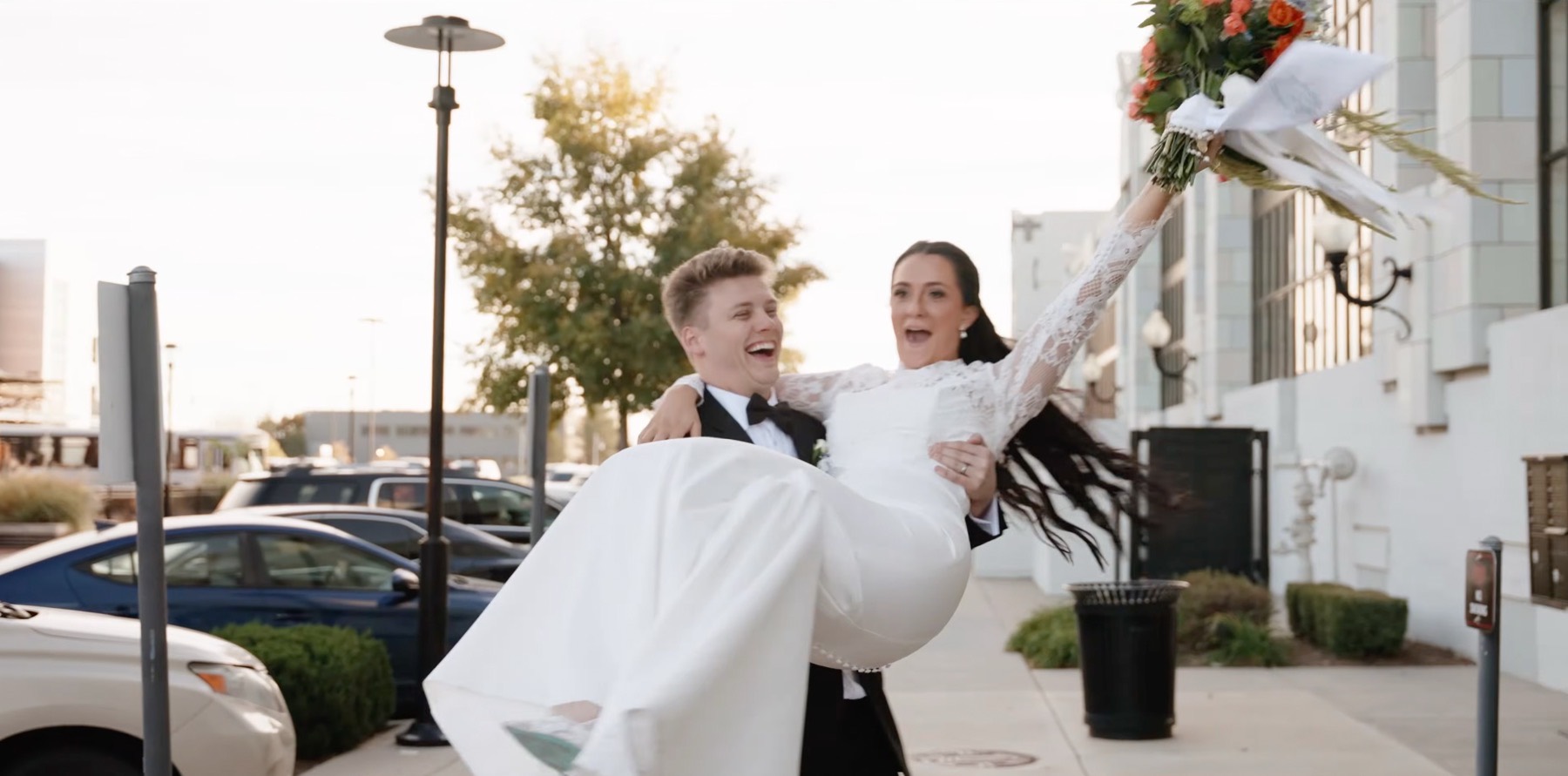 Groom carrying the bride down the street, her bouquet raised above them