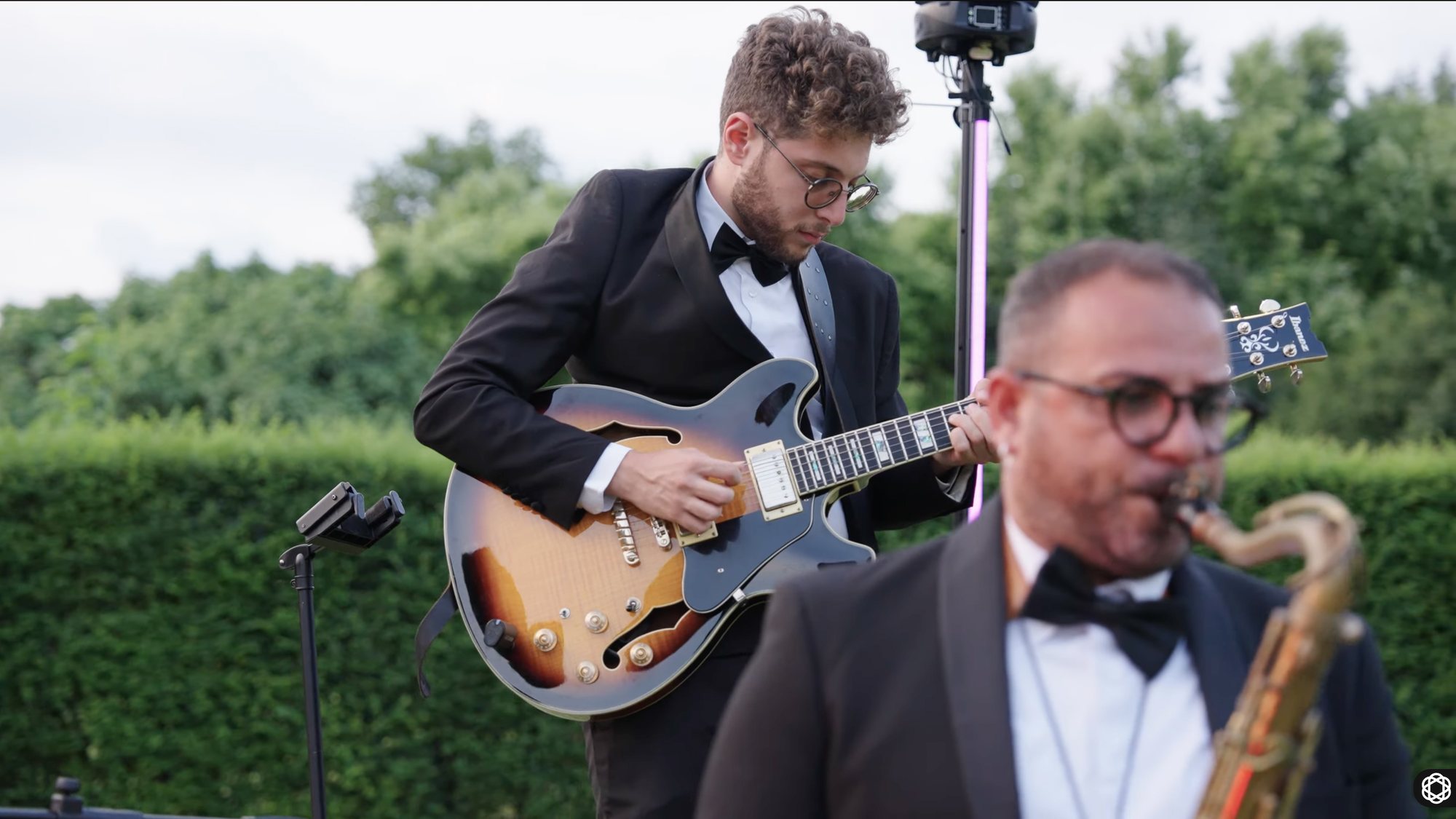 Two musicians in black tie playing guitar and saxophone at a wedding reception