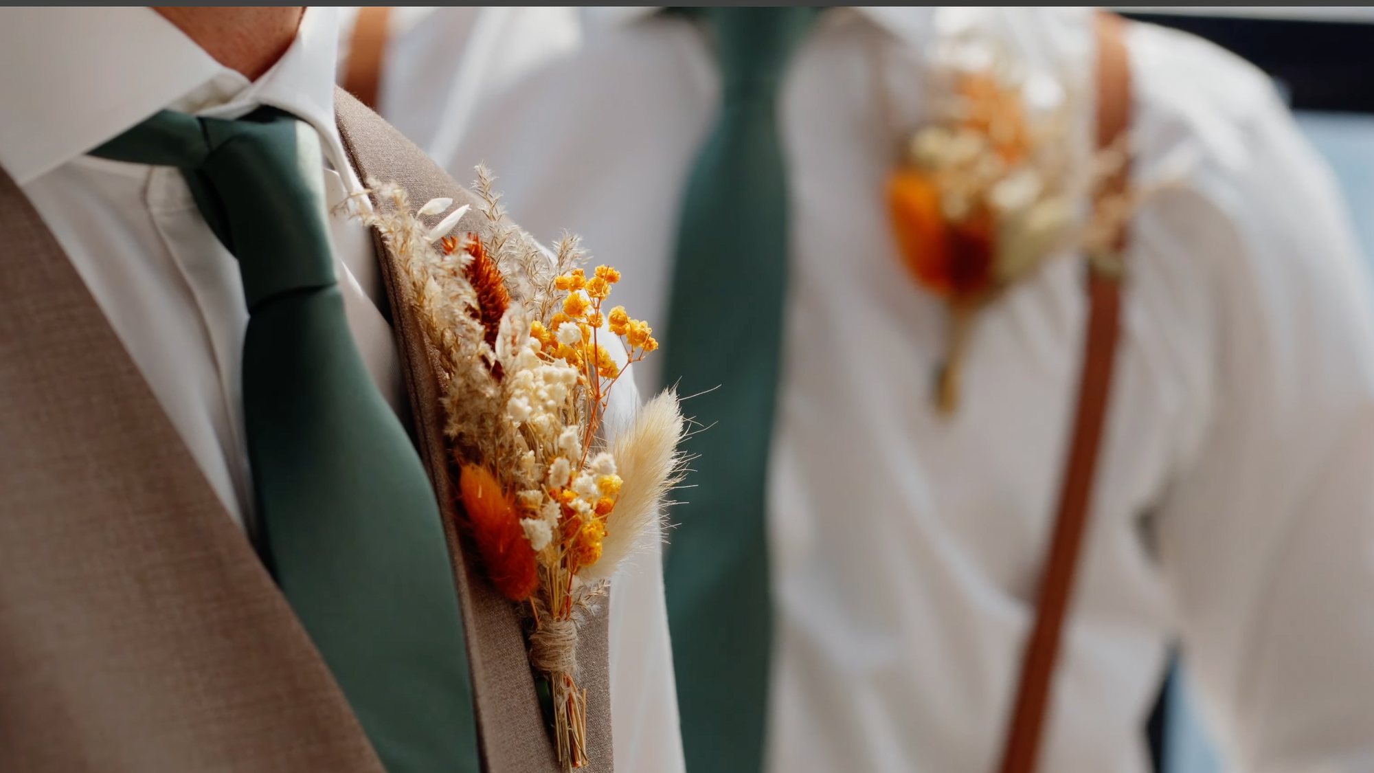Close-up of two buttonholes of dried flowers pinned over green ties