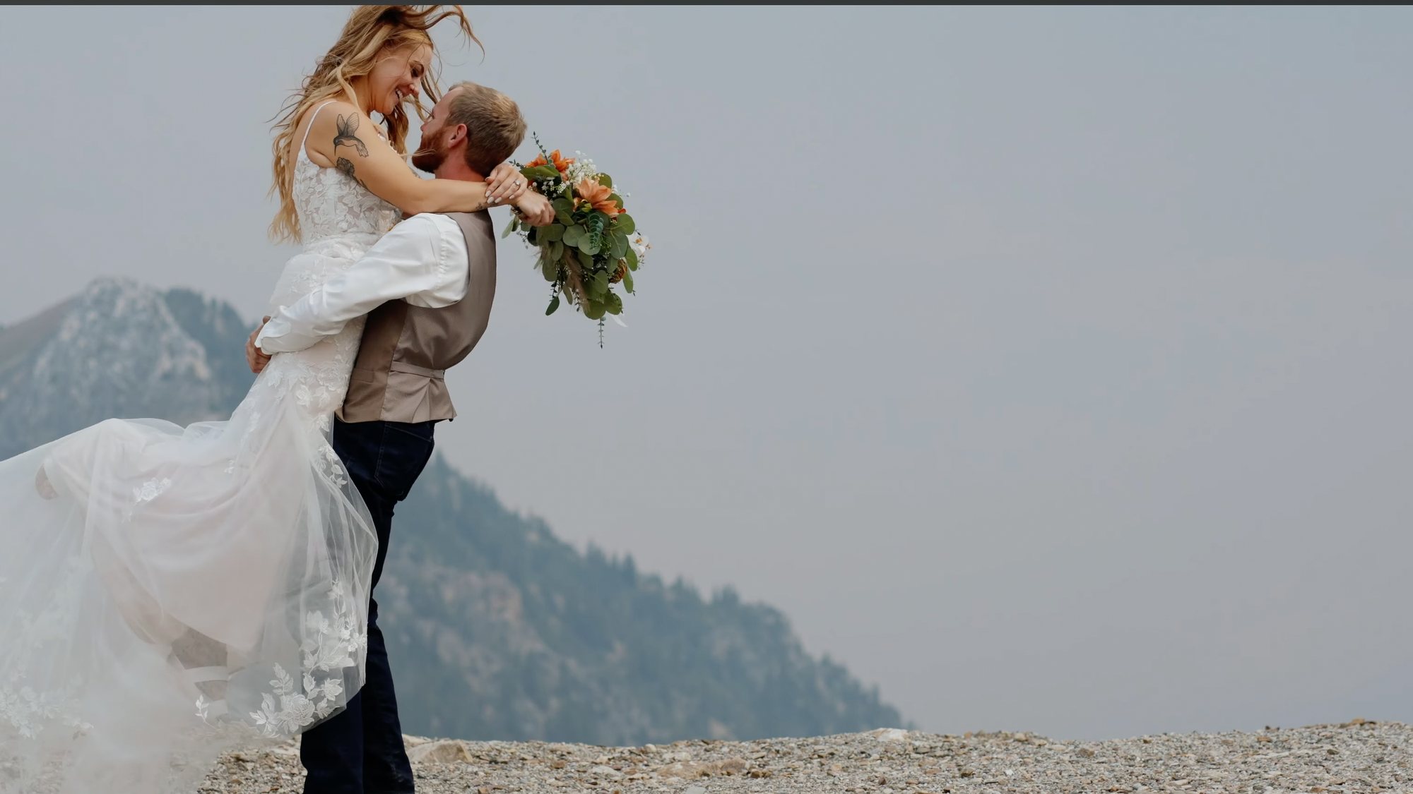 Groom lifting the bride off her feet on a clifftop terrace, a lake and mountains behind them